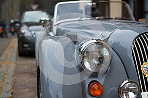 Close up of the headlight of a grey classic sport car, with blurred background