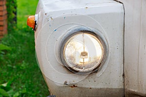 Close up of the headlight of an old abandoned truck with rusted white panels