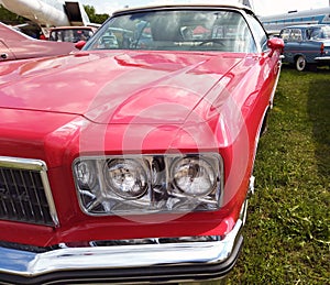 Close up, headlights of a shiny red classic car with focus on headlights and hood