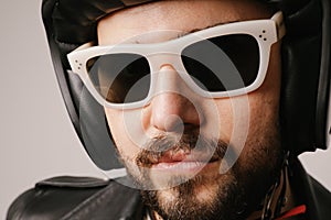 Close-up headshot of bearded biker man posing in leather jacket and sunglasses.