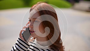 Close-up headshot of cheerful young woman talking on mobile phone outdoors in sunny summer day. Closeup portrait of