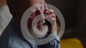 Close-up headshot of handsome gray-haired senior adult male talking on mobile phone with family at home in dark room.