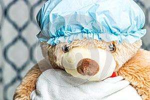 Close up headshot of a teddy bear in a shower cap and wrapped in a towel