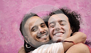 Close up headshot of two gay men lovers hug each other with smiles on their faces  on pink background