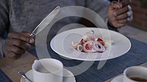 Close-up healthful salad in white dinner plate with African American male hands holding fork and knife dining in