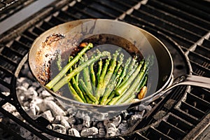 Close-up of healthy frying green asparagus with butter and garlic on carbon steel frying pan. Outdoor BBQ grill