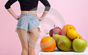 Close up of healthy girl with perfect buttocks and thighs. Beautiful legs near apple, orange and pear. Grey background. Fruits for