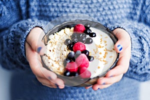 Close up of healthy organic breakfast. Child in woolen classic blue colored sweater holding bowl of of muesli and yoghurt with