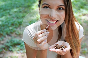 Close-up of healthy woman eating pecan nuts in the park. Looks at camera