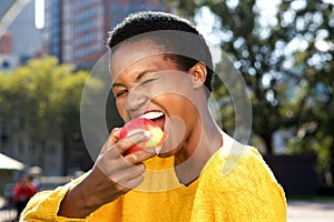 Close up healthy young black woman eating apple outdoors