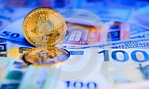 Close up heap of golden bitcoin physical coins on top of Euro, dollar banknotes background, high angle view, selective