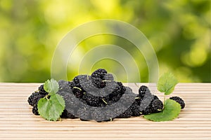 Close-up heap of ripe black mulberries with green leaves on table.