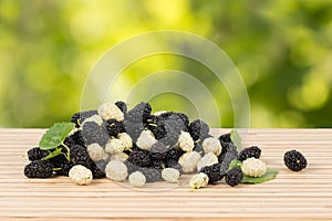 Close-up heap of ripe white and black mulberries with green leaves on table.