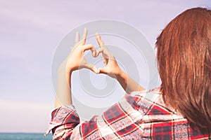 Close up of heart made by female hands background the turquoise ocean.