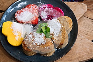 Close up heart shaped pancakes and tropical fruits on a black plate with mint and honey on wooden table. Valentine& x27;s