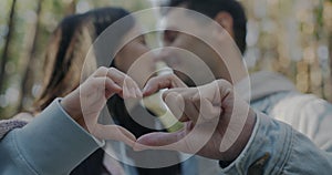 Close-up of heart symbol made with hands and blurred couple man and woman kissing outdoors