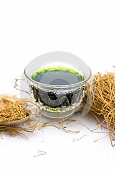 Close up of herbal and beneficial detoxifying tea of khus or vetiver grass in a glass cup with raw khus isolated.