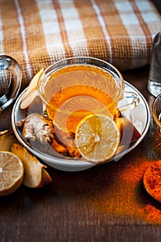 Close up of a herbal tea  consisting of apple juice,lemon,ginger and warm water in a transparent cup on a wooden surface in dark G