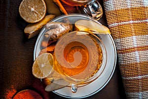 Close up of a herbal tea  consisting of apple juice,lemon,ginger and warm water in a transparent cup on a wooden surface in dark G