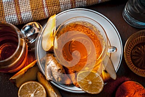 Close up of a herbal tea  consisting of apple juice,lemon,ginger and warm water in a transparent cup on a wooden surface in dark G