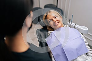 Close-up high-angle view of happy young woman patient with dental problem talking with unrecognizable dental doctor