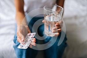 Close-up high-angle view of unrecognizable young woman holding pill in hand with water. Female going to take tablet from