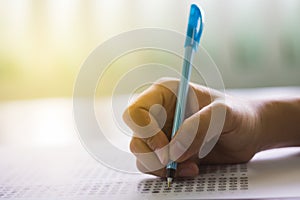 Close up of high school or university student holding a pen writing on answer sheet paper in examination room. College students an