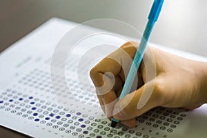 Close up of high school or university student holding a pen writing on answer sheet paper in examination room. College students an