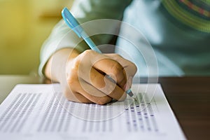 Close up of high school or university student holding a pen writing on answer sheet paper in examination room. College students an