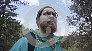 Close up of hipster hiker observing the the green valley on blue cloudy sky background. Stock footage. A bearded man