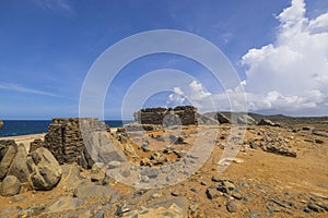 Close up historical view of Caribbean coastline with ruins of gold smelter Bushiribana against blue sky with white clouds.
