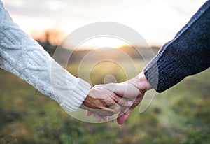 A close-up of holding hands of senior couple in an autumn nature at sunset.