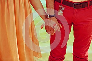 Close up holding hands together of young couple og hipsters in love. Stylish trendy clothes. Peach and red colors. Vintage style.