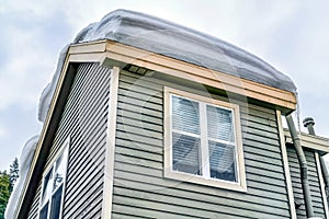 Close up of home exterior with thick snow on the roof and horizontal wall siding