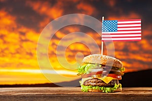 Close-up home made beef burger with american flag on the top on wooden table over sunset sky background