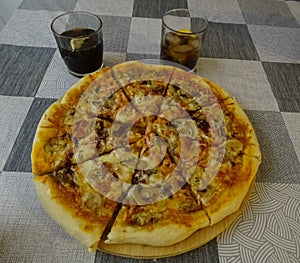 Close-up of a homemade bacon pizza, extra cheese and mushrooms and two glasses of soda