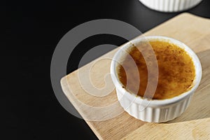Close up homemade creme brulee in white ramekin  with sugar burn top up on black background with copy space. French dessert creme