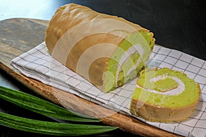 Close up of homemade Pandan Jam Roll Cake with white cream inside, on wooden board on black table background. Foods and drinks