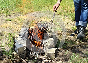 Close-up of a homemade stone grill and a man`s hand throwing firewood. Light a fire on the grill