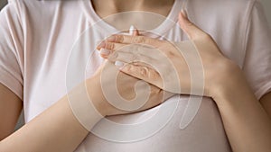 Close up hopeful beautiful young woman keeping hands on chest