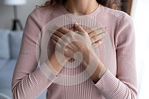 Close up hopeful grateful young woman keeping hands on chest