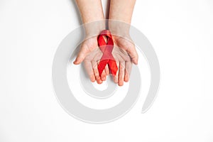 Close up horizontal image of child`s hands holding red ribbon on white background, HIV awareness concept, world AIDS day.