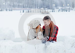 Close-up horizontal portrait of the happy beautiful couple funnily talking while building the snowman in the countryside