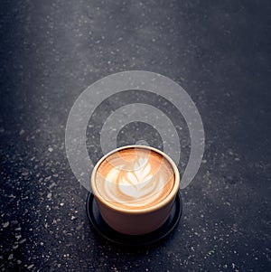 Close up hot capucino coffee cup with latte art foam on black stone table at cafe.dark scene.banner space mock up for adding text