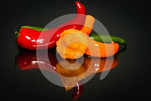 Close-up of hot chili peppers lying ob black reflectin background