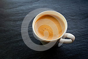 Hot coffee cup with foam crema on a stone board back color with copy space photo