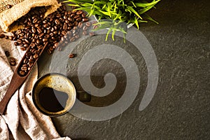 Close-up of Hot coffee for morning with milk foam in matte black ceramic cup and napkin with coffee beans roasted in sack on dark