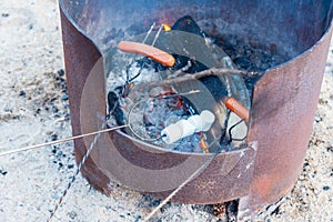 Close-up of hot dogs and marshmallows cooking on roasting sticks over campfire