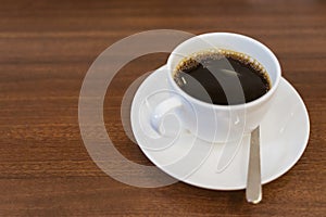 Close up hot espresso with bubbles in white coffee cup on wood table near window in coffee shop in the morning in vintage soft