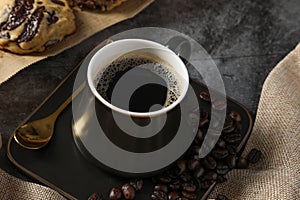 Close up Hot fresh black coffee in a luxury black cup with foam and coffee beans on black table background. Drink concept